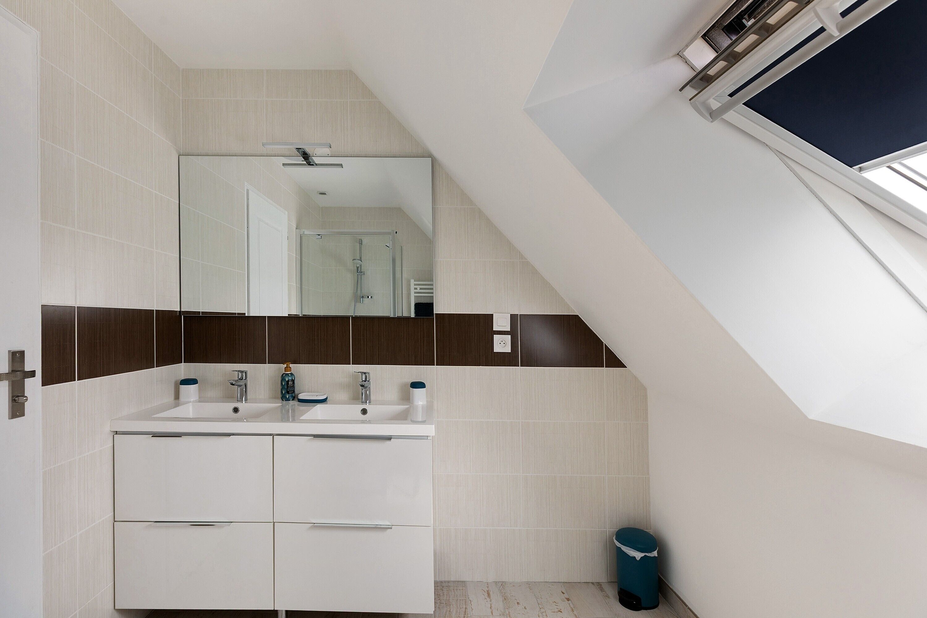 Un baño moderno con un tocador blanco, un espejo grande y una ventana sobre el lavabo.