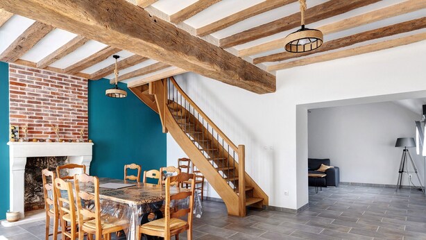 A dining area with a brick wall, wooden staircase, and a table with chairs.