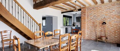 A dining area with a wooden table and chairs, a staircase, and exposed wooden beams.