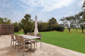 Un patio al aire libre con una mesa y sillas, una sombrilla y un césped.