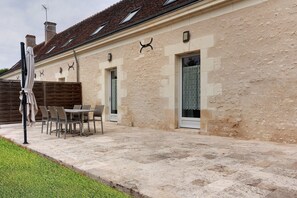 A building with a stone facade, a tiled roof, and a patio area with a table and chairs.