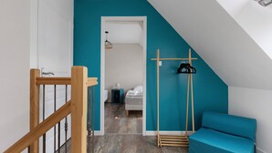 Ein Zimmer mit einer Wand in Türkis, einer Holztreppe, einem Bett, einer Hängelampe und einem blauen Sessel.