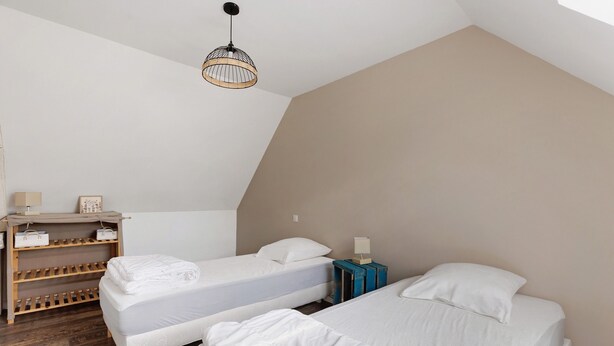 Ein Zimmer mit zwei Betten, einem Holzbodenregal mit Taschen, einer Pendelleuchte und einem kleinen Tisch mit einer Lampe.