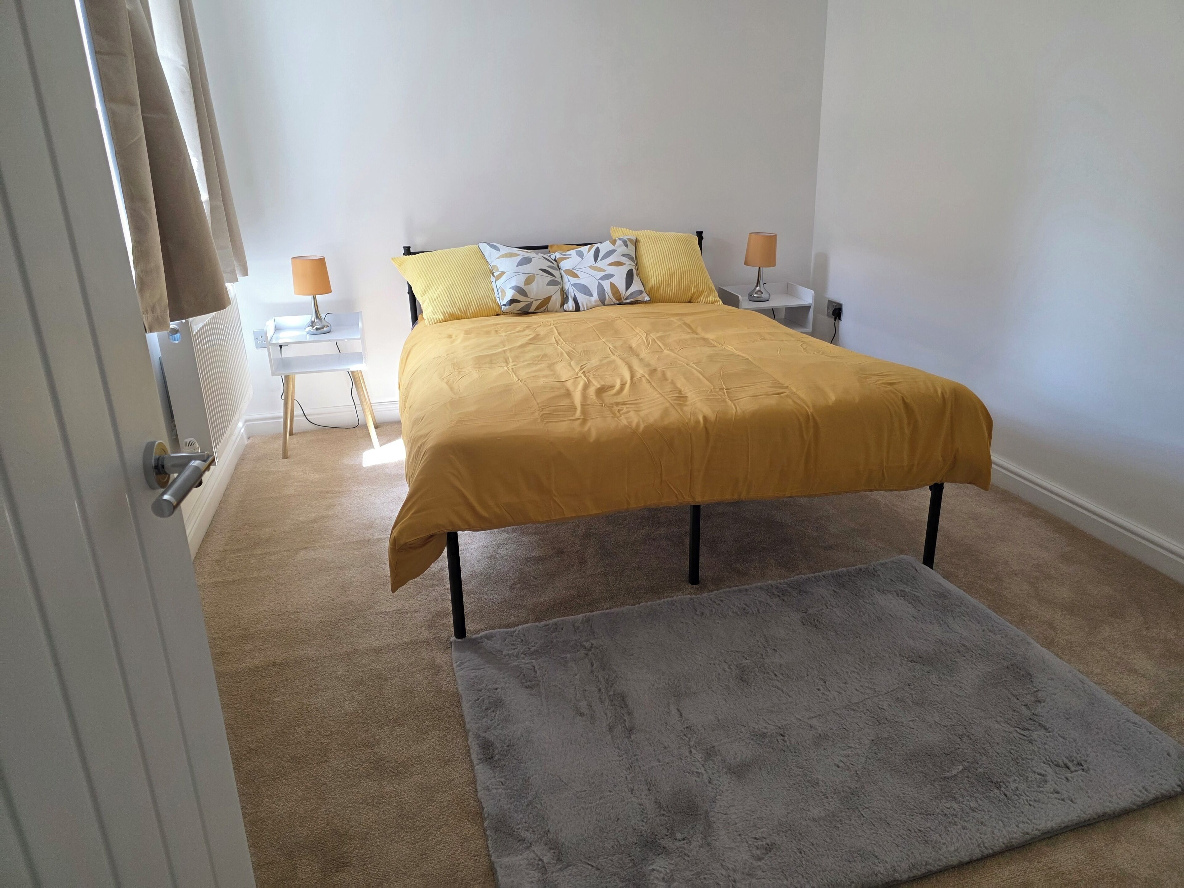 Ein Schlafzimmer mit einem Bett, zwei Nachttischlampen, einem Heizkörper, einem grauen Teppich und einer Tür.