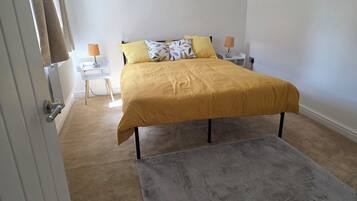 Ein Schlafzimmer mit einem Bett, zwei Nachttischlampen, einem Heizkörper, einem grauen Teppich und einer Tür.
