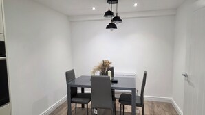 A dining area with a rectangular table, four chairs, a vase with dried plants, and pendant lighting. - Luxury retreat In the heart of St Neots, free parking and close to town centre (St. Neots)