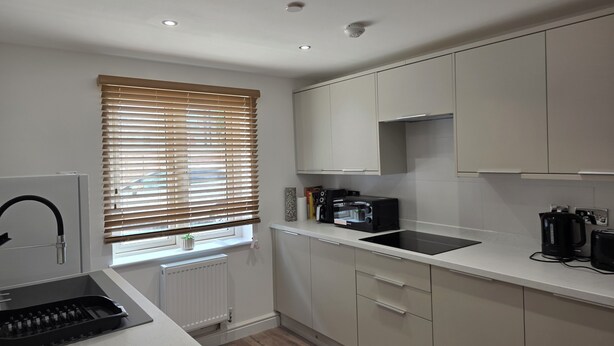 A modern kitchen with white cabinets, a black induction cooktop, and a window with blinds. - Luxury retreat In the heart of St Neots, free parking and close to town centre (St. Neots)
