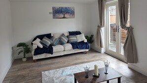 A living room with a sofa, a painting, a potted plant, a table with candles, and a sliding glass door. - Luxury retreat In the heart of St Neots, free parking and close to town centre (St. Neots)