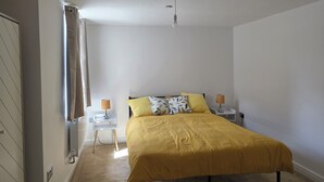 A bedroom with a bed, two bedside tables with lamps, a radiator, and a window with curtains. - Luxury retreat In the heart of St Neots, free parking and close to town centre (St. Neots)
