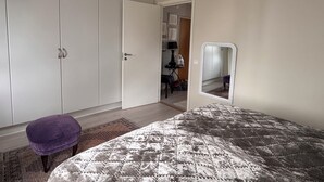 Une chambre à coucher avec un lit, une armoire, un miroir et un petit tabouret.