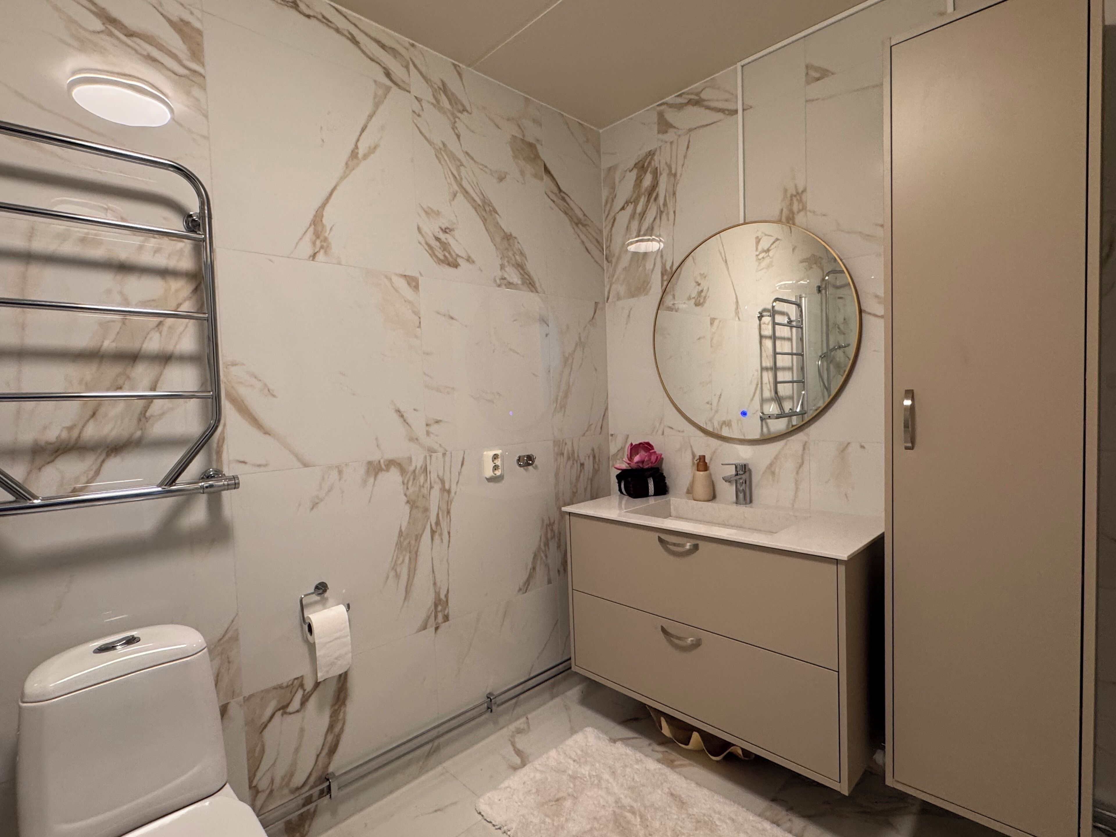 Een badkamer met toilet, handdoekhouder, wastafel met spiegel en kast.