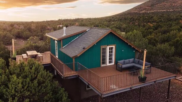 A single-story house with a deck, surrounded by dense forest, and a clear sky. - Wrap-around deck, cozy home, gateway to the Canyon. (Williams)