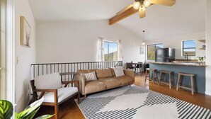 A spacious living area with a sofa, a dining table, and a kitchen area with a refrigerator and bar stools. - Wrap-around deck, cozy home, gateway to the Canyon. (Williams)