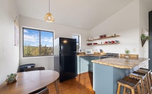 A modern kitchen with a black refrigerator, a dining table, and bar stools. - Wrap-around deck, cozy home, gateway to the Canyon. (Williams)