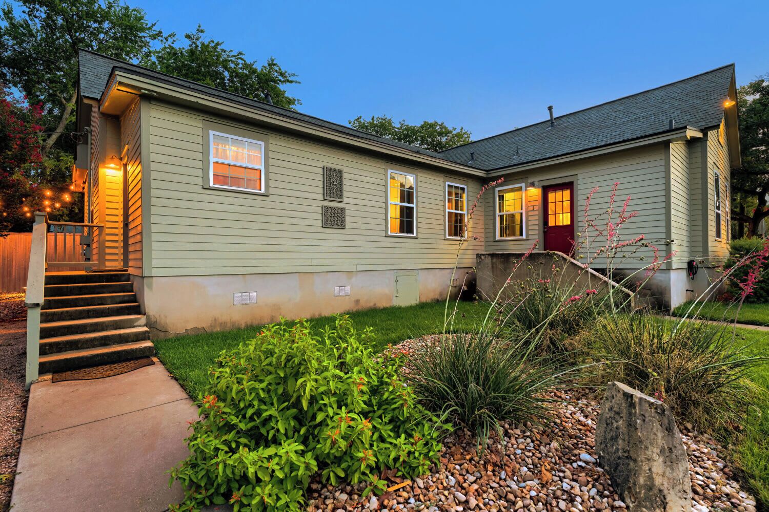 A two-story house with a front porch, a set of stairs leading up to the entrance, and a well-maintained garden with various plants and a gravel pathway.
