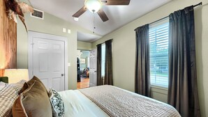 Ein Schlafzimmer mit Bett, Deckenventilator, Tür und einem Fenster mit Vorhängen.