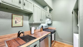 A compact kitchen with a wooden countertop, a sink, a stove, and light green cabinets.