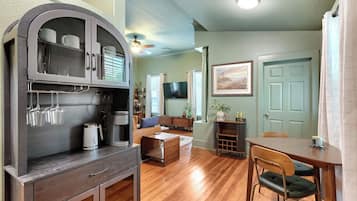 A living room with a sofa, coffee table, and a TV. There is a dining area with a table and chairs.