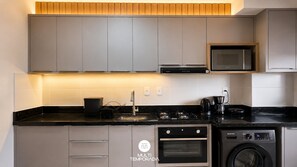 A modern kitchen with grey cabinets, a microwave, a stove, a coffee maker, and a washing machine. - Skyline Comfort Club - Elegance - Penha/sc (Penha)