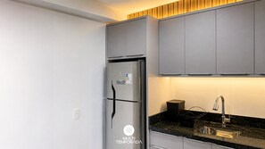 Une cuisine moderne dotée d’un réfrigérateur encastré en acier inoxydable, de meubles de rangement gris, d’un plan de travail noir et d’un évier en acier inoxydable.