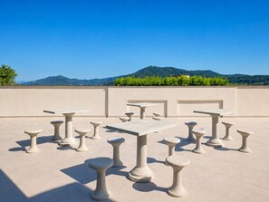 Une terrasse sur le toit, dotée de nombreuses tables et de tabourets, un ciel dégagé et un paysage montagneux en toile de fond.