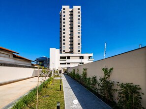 A modern building with a central staircase leading to an upper level, surrounded by a landscaped area with plants and a paved walkway. - Skyline Comfort Club - Elegance - Penha/sc (Penha)