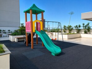Un espace de jeux pour enfants avec un toboggan et des structures d’escalade, situé sur une terrasse sur le toit.