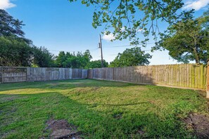 A backyard with a wooden fence, a grassy lawn, and trees. - Family Getaway: 4BR, BBQ Yard, Steps to Park (La Porte)