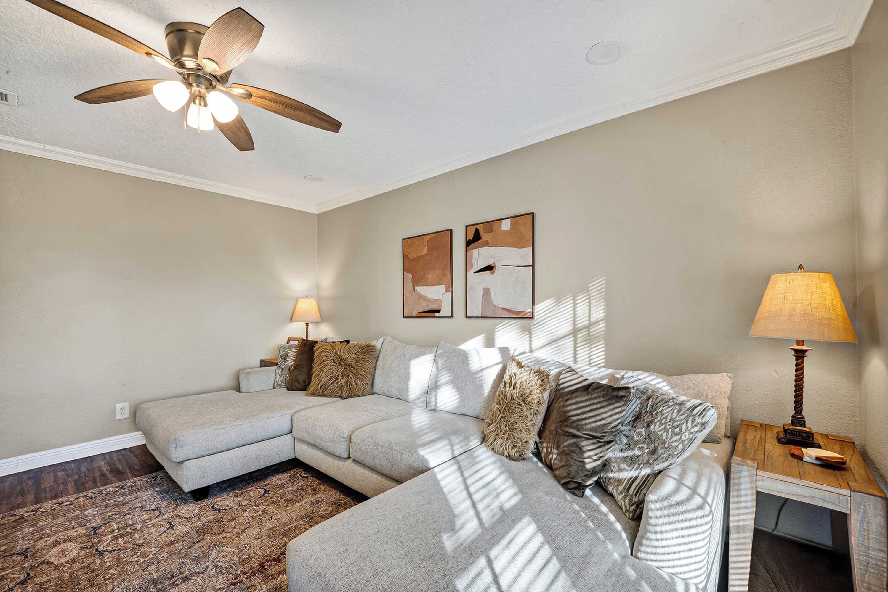 A modern living room with a sectional sofa, a ceiling fan, and artwork on the wall.