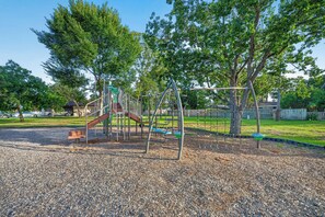 Ein Spielplatz mit Rutsche und Klettergerüsten, umgeben von Bäumen und einer Schotterfläche.