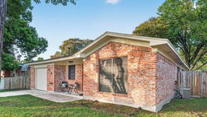 A single-story brick house with a covered patio, a fenced yard, and a large window. - Family Getaway: 4BR, BBQ Yard, Steps to Park (La Porte)