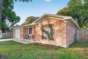 A single-story brick house with a covered patio, a fenced yard, and a large window. - Family Getaway: 4BR, BBQ Yard, Steps to Park (La Porte)