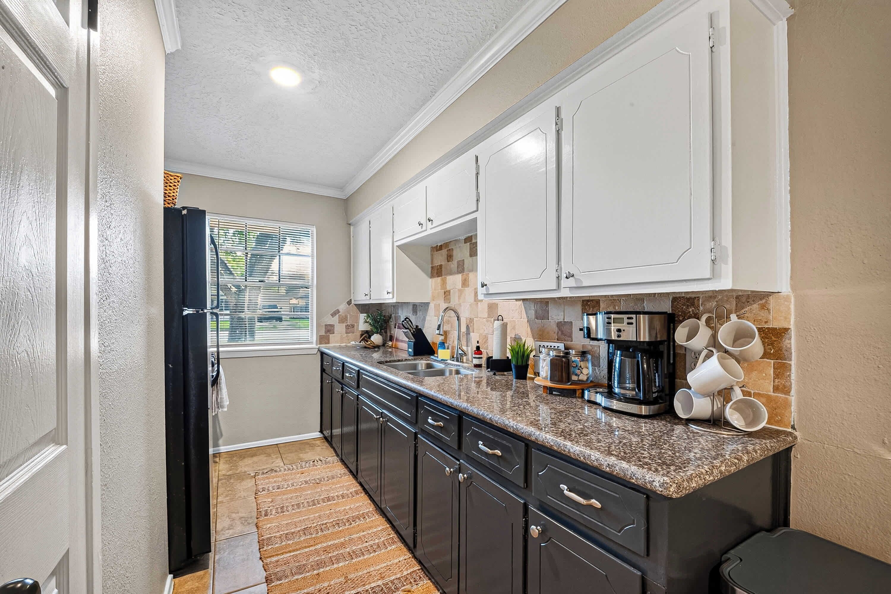 A kitchen with dark cabinets, a granite countertop, a coffee maker, and a window with blinds.