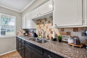A kitchen with granite countertops, a double sink, and a backsplash of brown and beige tiles. - Family Getaway: 4BR, BBQ Yard, Steps to Park (La Porte)