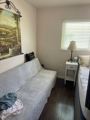 A bedroom with a bed, a nightstand, a lamp, a painting, and a window with blinds. - Fabulous 2-bedroom apartment in sunny San Clemente perfect for relaxing (San Clemente)