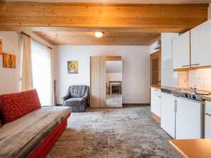 Ein Zimmer mit einer Couch, einem Sessel, einem Esstisch und einer Küchenzeile.
