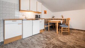 A compact kitchen with white cabinets, a wooden countertop, and a dining area with a bench and table. - Appartements Sonnberg - Top 1 (Bad Hofgastein)