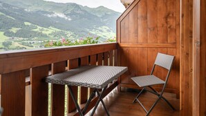A wooden balcony with a table and chair, overlooking a mountainous landscape. - Appartements Sonnberg - Top 1 (Bad Hofgastein)