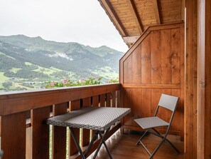 Ein Holzbalkon mit Tisch und Stuhl, mit Blick auf eine gebirgige Landschaft.