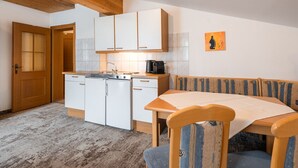 A compact kitchen with white cabinets, a wooden ceiling, and a dining area with a table and chairs. - Appartements Sonnberg - Top 1 (Bad Hofgastein)