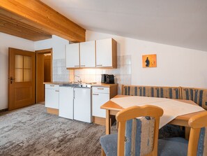 Eine kleine Küche mit weißen Schränken, Holzbalkendecke und einem Essbereich mit Tisch und Stühlen.