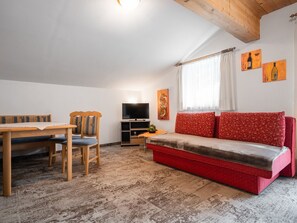 A cozy living room with a wooden dining table, two chairs, a red sofa, a television, and artwork on the walls. - Appartements Sonnberg - Top 1 (Bad Hofgastein)