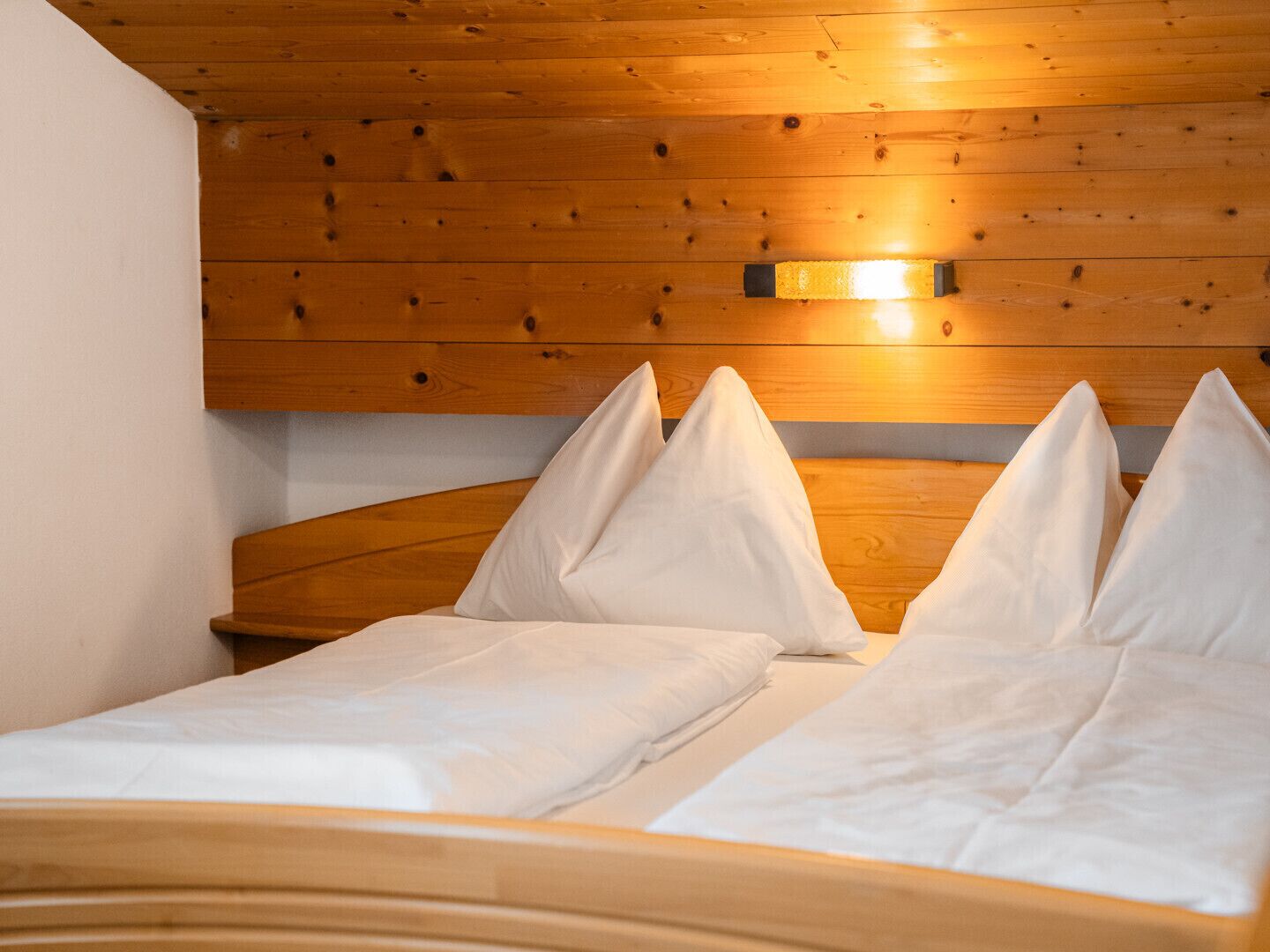 Ein Zimmer mit zwei Einzelbetten, einem Holzkopfteil und einer wandmontierten Lampe.