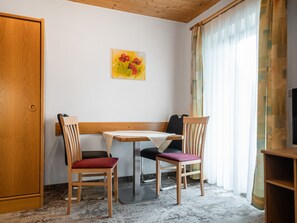 A small room with a wooden door, a bench, two chairs, a table, a painting, and a window with curtains. - Appartements Sonnberg - Top 2 (Bad Hofgastein)