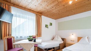 Una habitación con techo de madera, una cama, un escritorio con silla, un televisor y una ventana con cortinas.