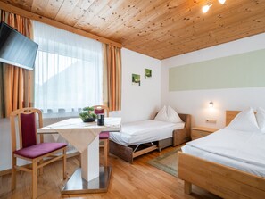 Ein Zimmer mit Holzboden, einem Bett, einem Schreibtisch mit Stuhl, einem Fernseher und einem fenster mit Vorhängen.