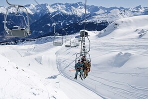 Eine Seilbahn mit Skifahrern, die einen schneebedeckten Hang hinaufsteigen, umgeben von Bergen.