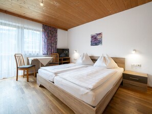Habitación de hotel con techo de madera, cama con ropa de cama blanca, escritorio con silla, televisor y una lámpara de pared.