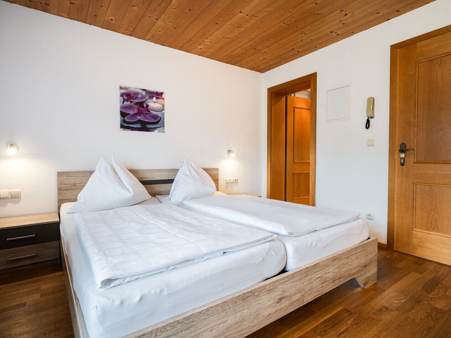 Un lit bien fait, avec du linge de lit blanc, dans une pièce au plancher et au plafond en bois.