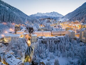 Un pueblo cubierto de nieve en la montaña, con edificios, una cascada y laderas boscosas.